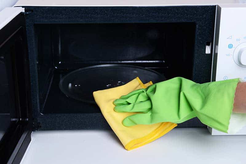 A person cleaning the inner part of a microwave