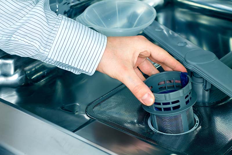 A person removing filter from dishwasher