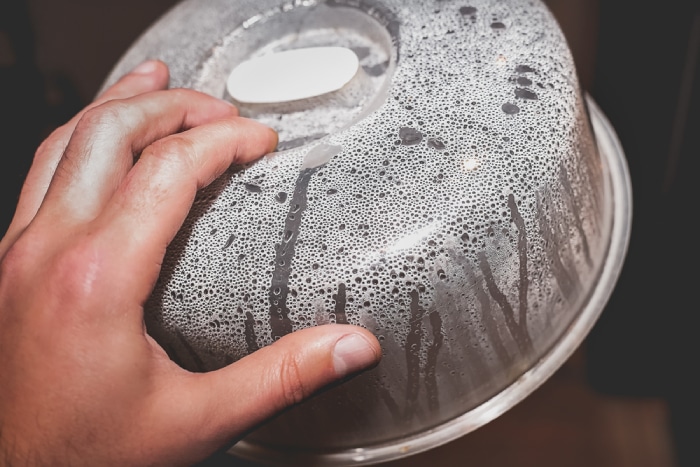 A hand holding a microwave cover with condensation