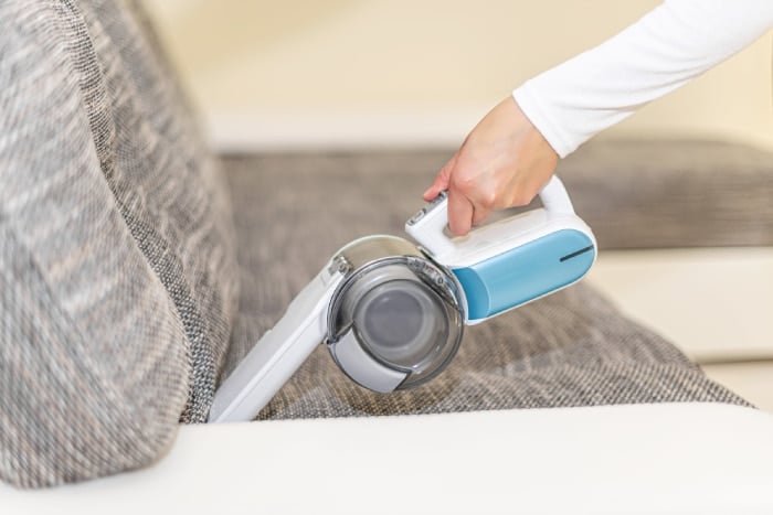 using handheld vacuum to clean sofa