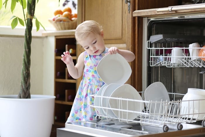 Baby girl playing with the crockery on the dishwasher