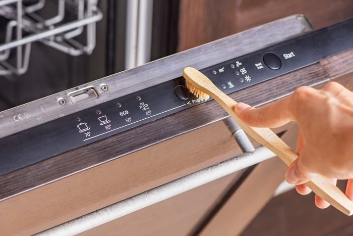 A person scrubbing away dirt from their dishwasher's control panel and buttons