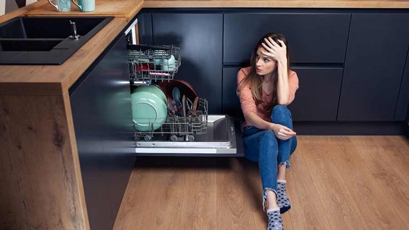 Young woman sitting next to her dishwasher.