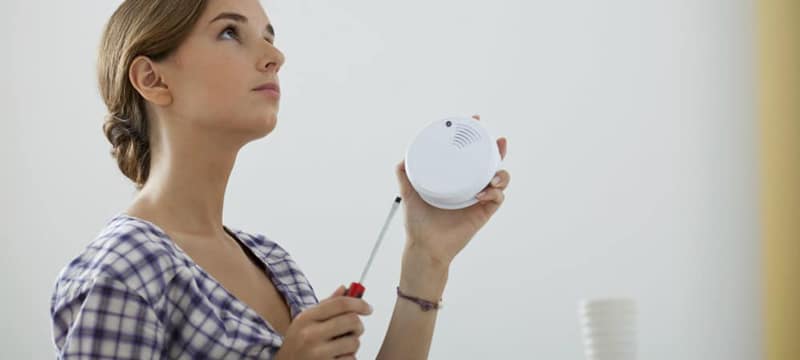 Woman holding a smoke detector and a screwdriver