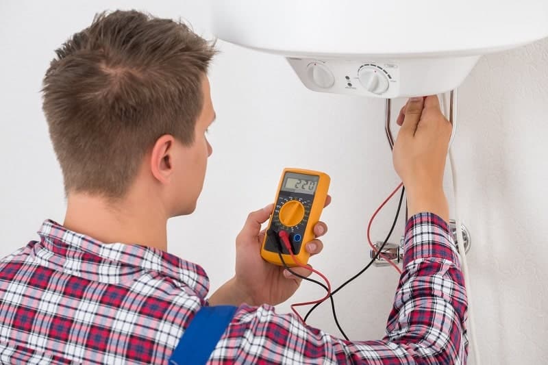A man testing the water heater's thermostat with a multimeter tool