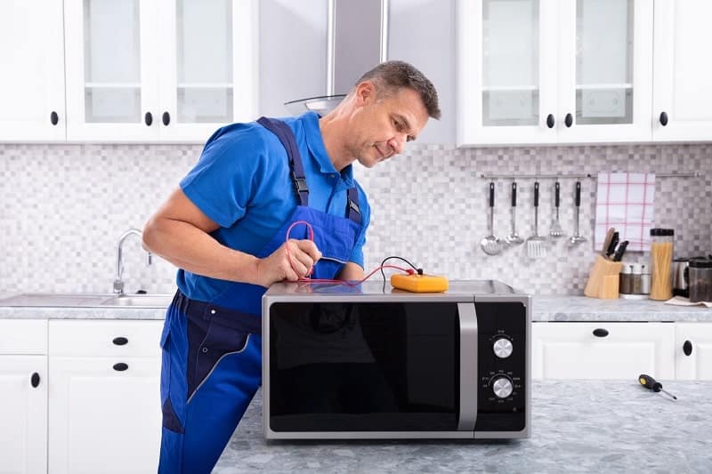 A man testing the microwave with a multimeter tool