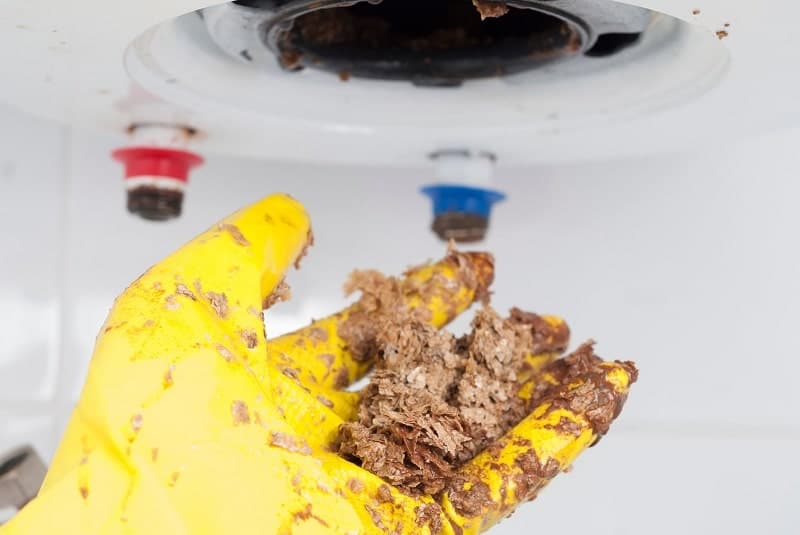 A hand getting the sediments from a water heater tank