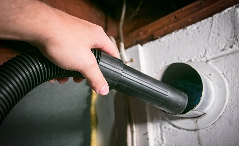 Hand using a vacuum to clean an exhaust duct