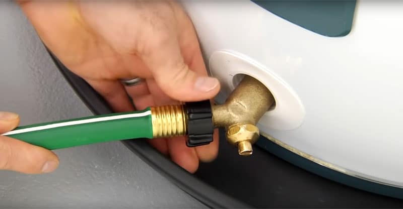Hands connecting a hose to a water heater drain system