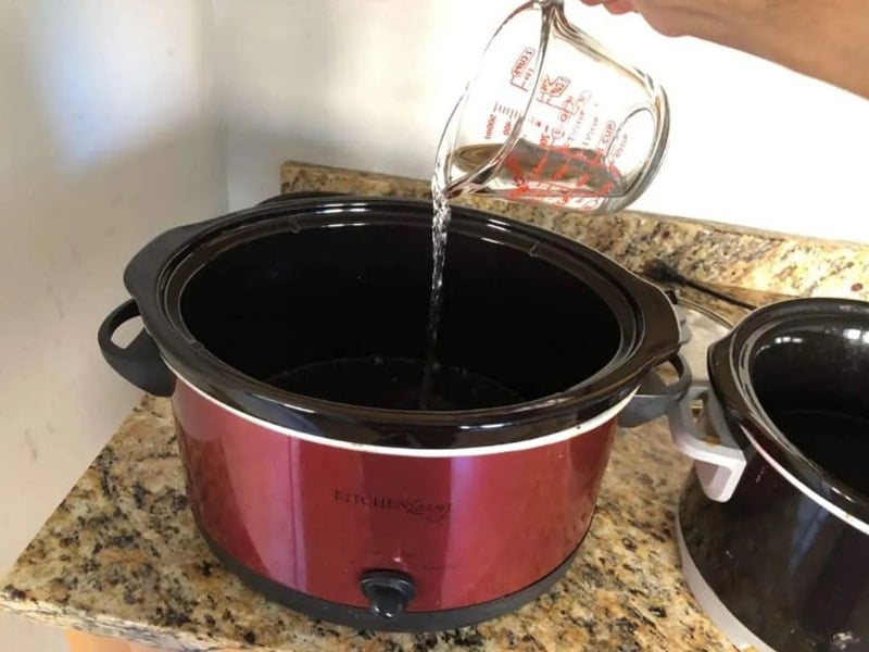 Hand filling slow cooker with water