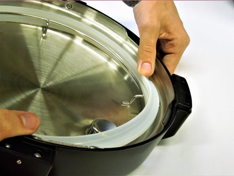Hands replacing lid sealing of slow cooker