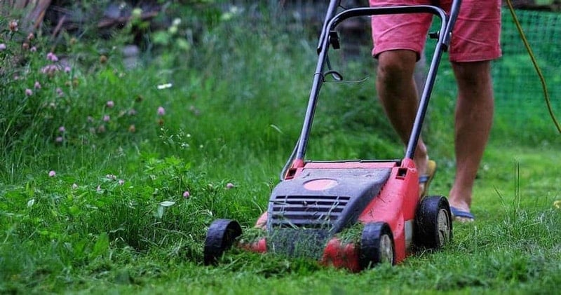Man using a lawn mower in wet grass