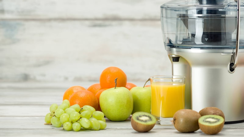 Juicer with a cup of juice and some fruits beside