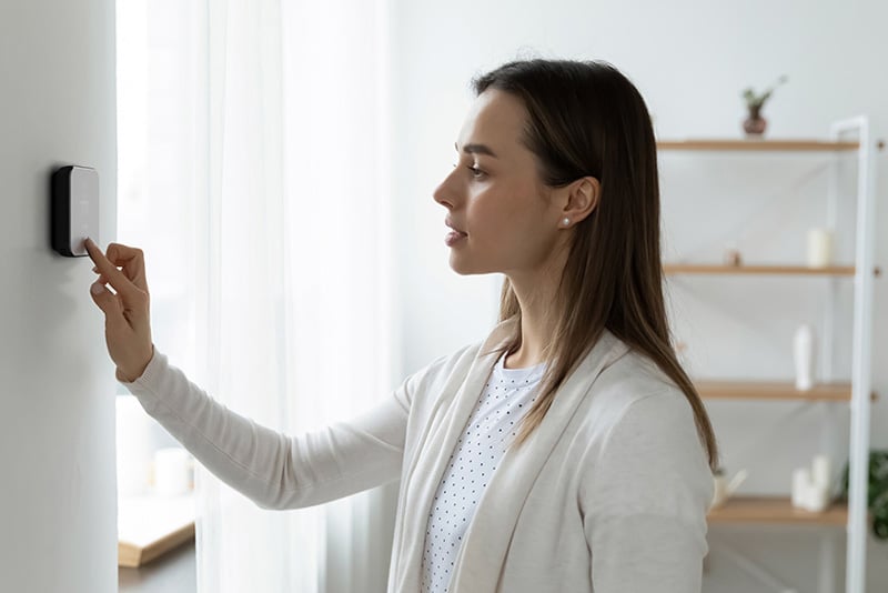 Woman Setting Thermostat Temperature