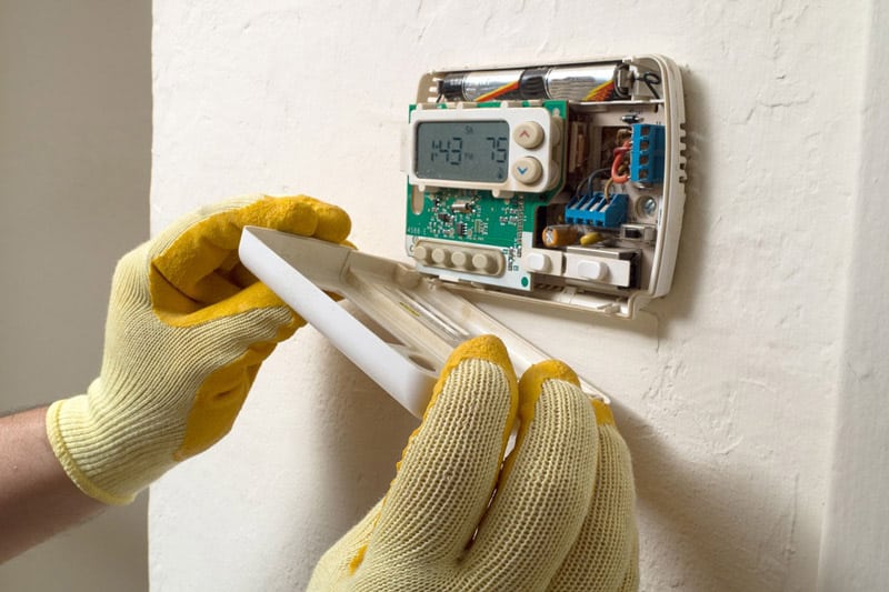 Hands with work gloves fixing Emerson Thermostat