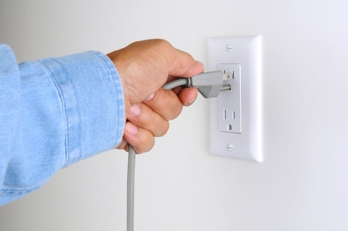 A man plugging a power cord into the wall