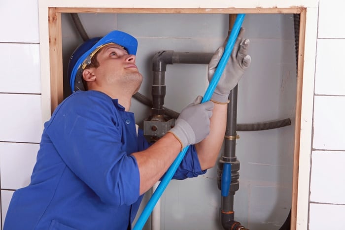 A plumber working on pipes behind a wall