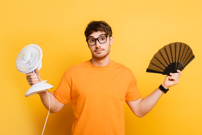 A young man holding a hand fan, and an electric one
