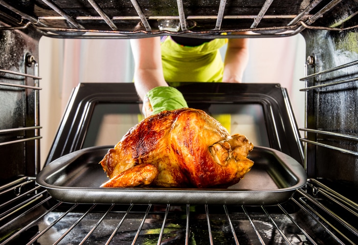 A person placing a chicken inside an oven