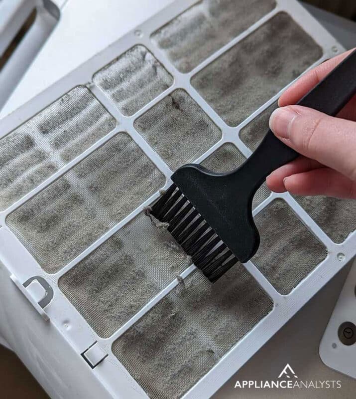Using a brush to clean dust from the air conditioner filter