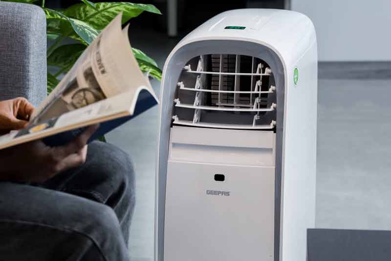 Man sitting in a armchair reading next to a portable air conditioner