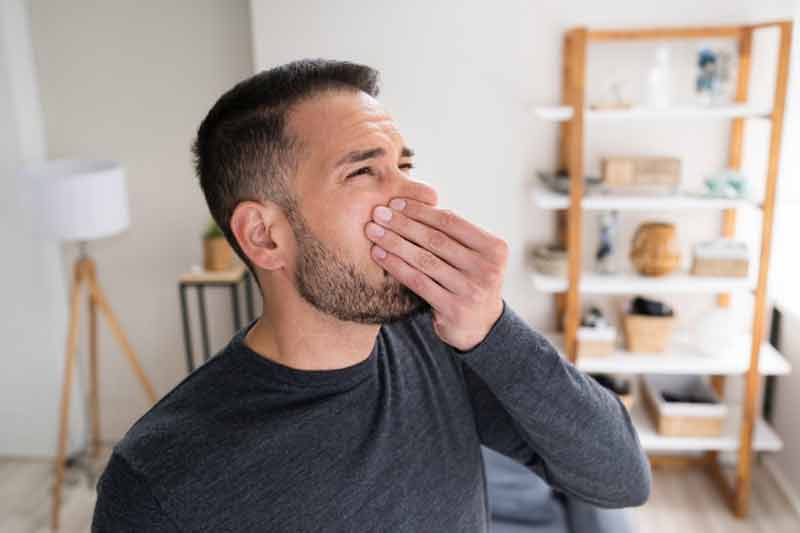 Man covering his nose due to the fishy smell coming from his window air conditioner.