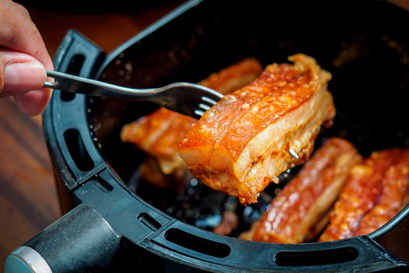 Hand removing a piece of greasy pork from the air fryer