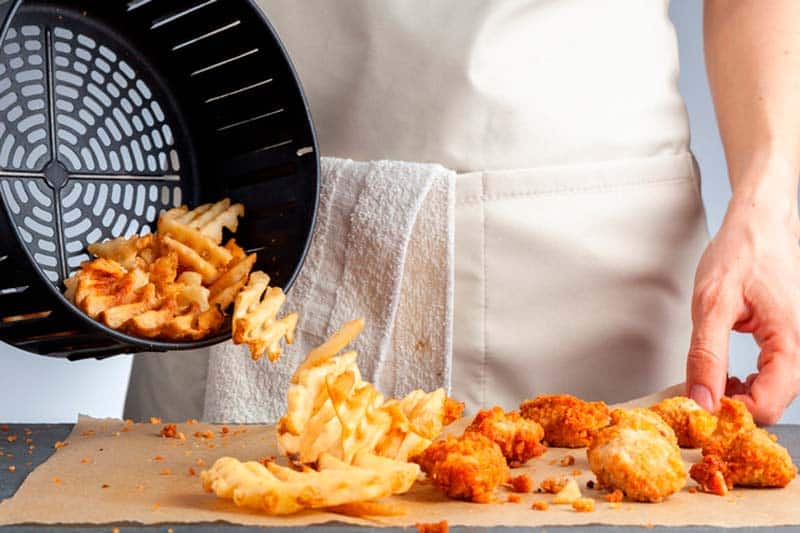 Person serving various fried foods on the table from an air fryer basket