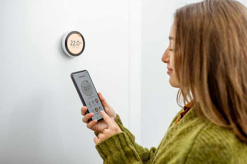 Woman Setting Thermostat With Her Cellphone